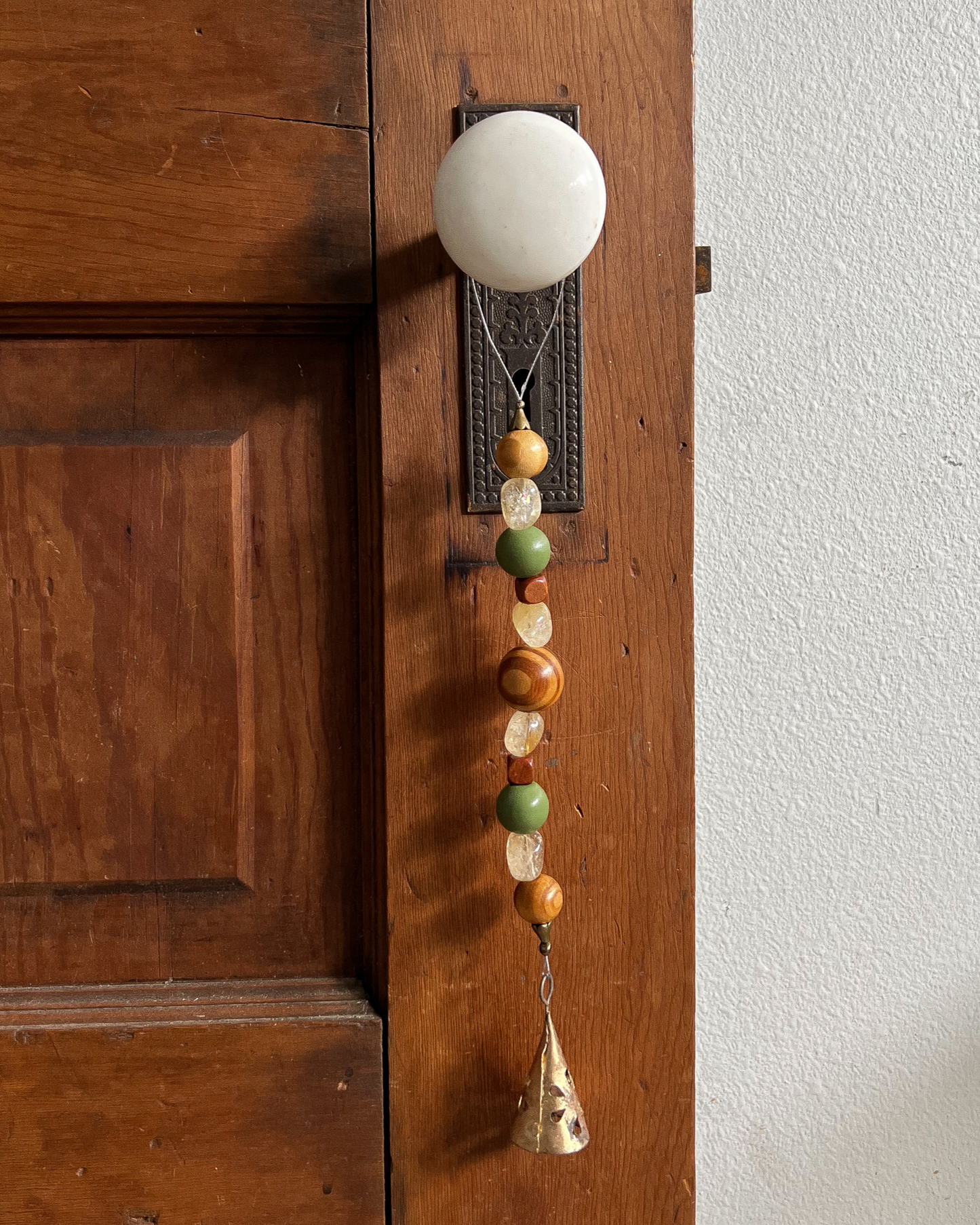 Single strand of wooden beads, citrine crystals, and a golden bell hang from an antique doorknob.