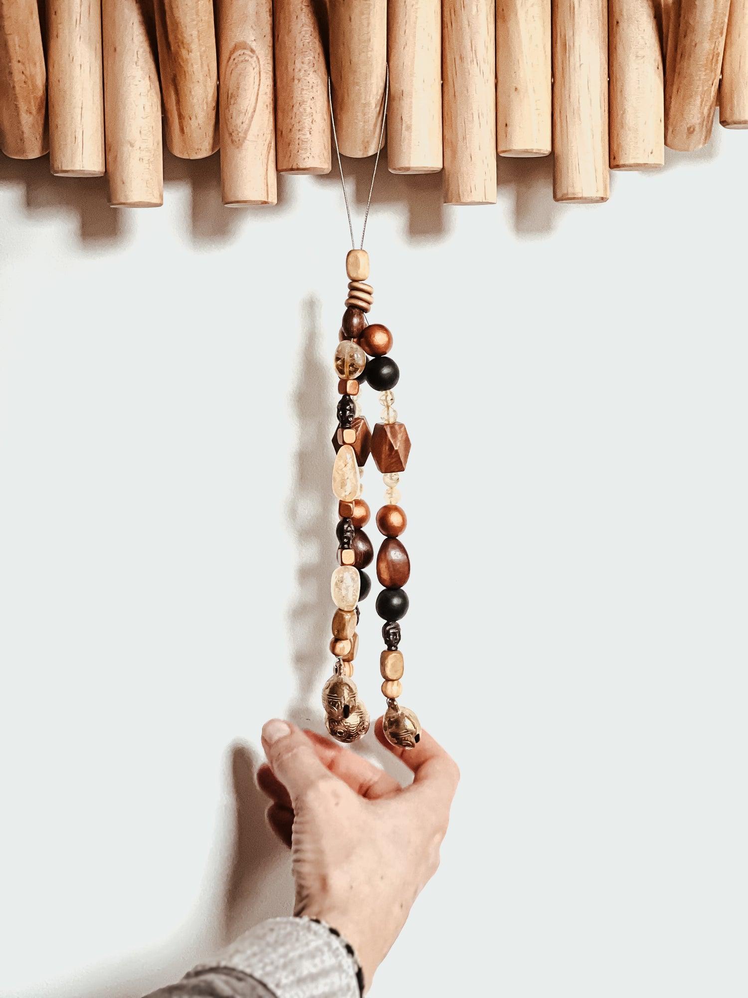 Photo of hand lightly ringing handcrafted bells attached to a triple strand of wooden beads, citrine crystals, and metal buddhas.