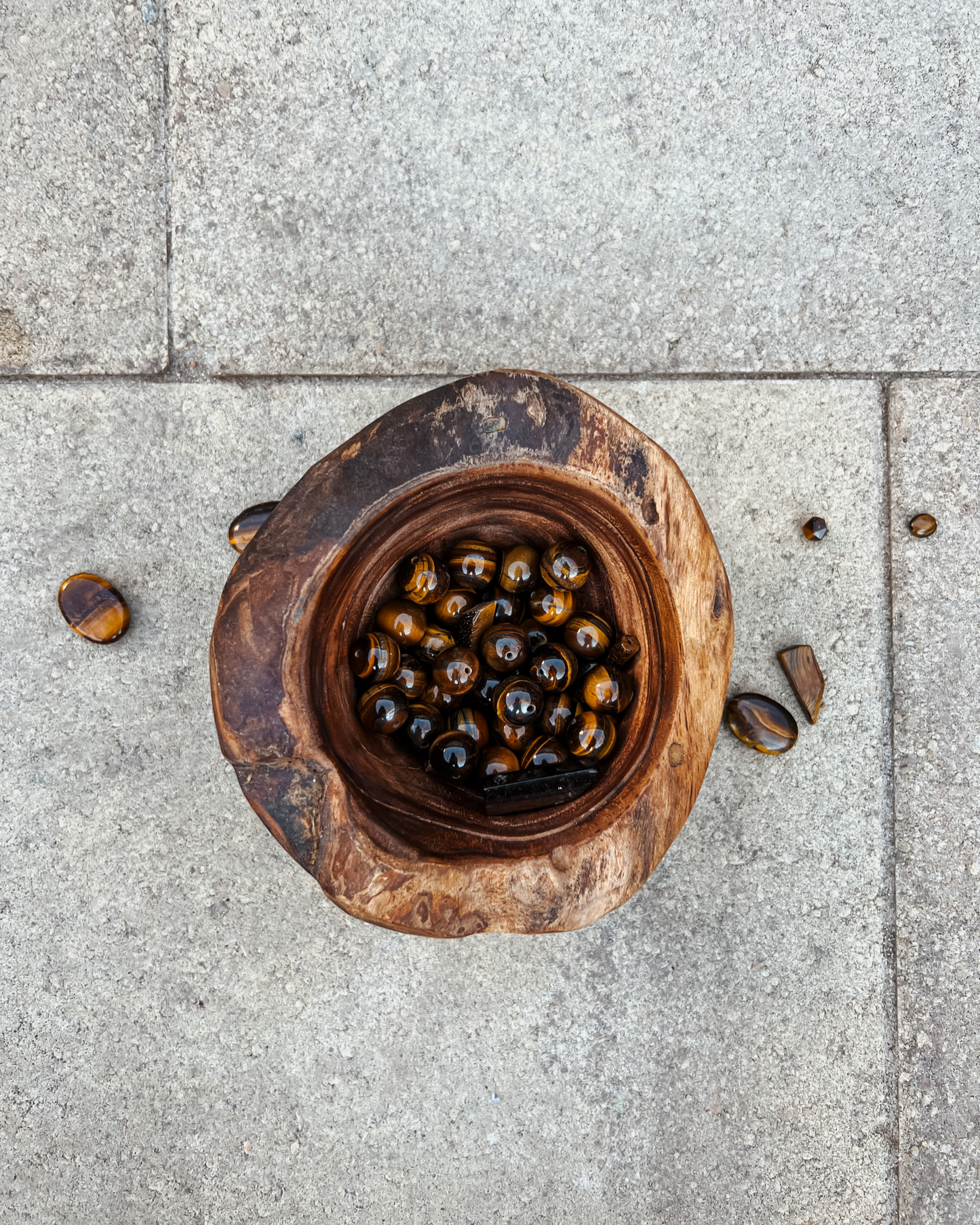 Photo of an overhead view of a wooden bowl full of tiger's eye crystals.