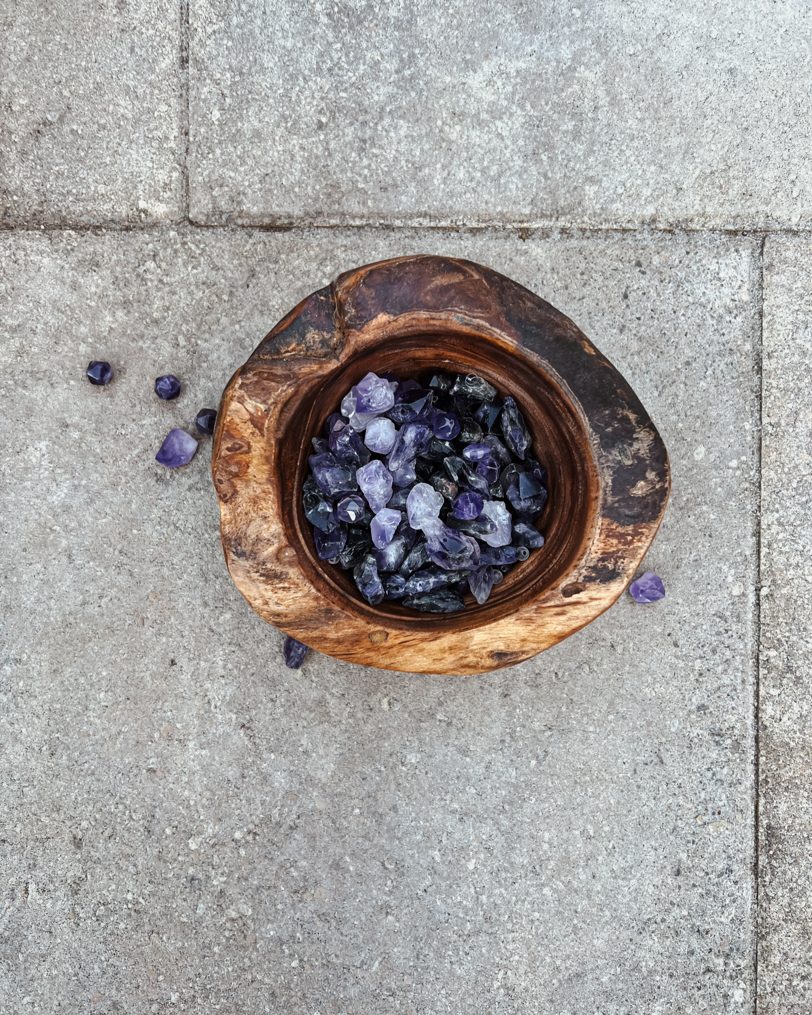 Photo of an overhead view of a wooden bowl full of amethyst crystals.