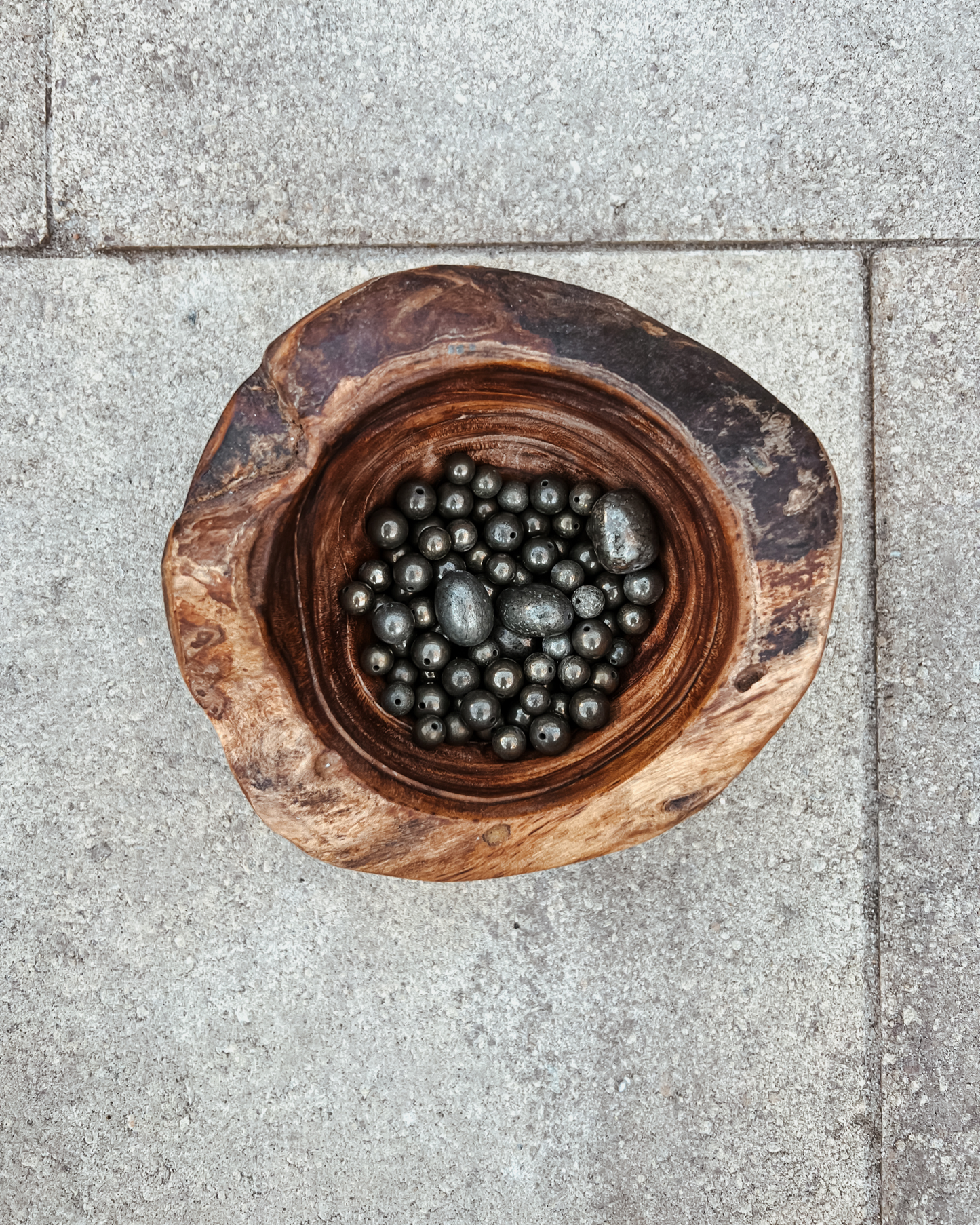 Photo of an overhead view of a wooden bowl full of pyrite crystals.