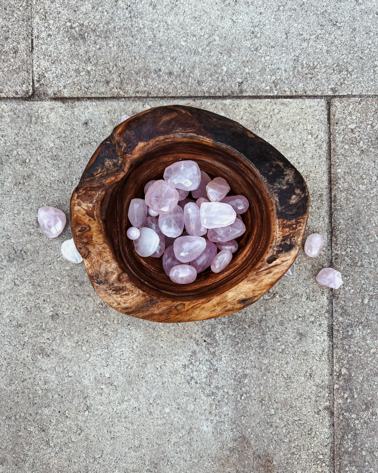 Photo of an overhead view of a wooden bowl full of rose quartz crystals.