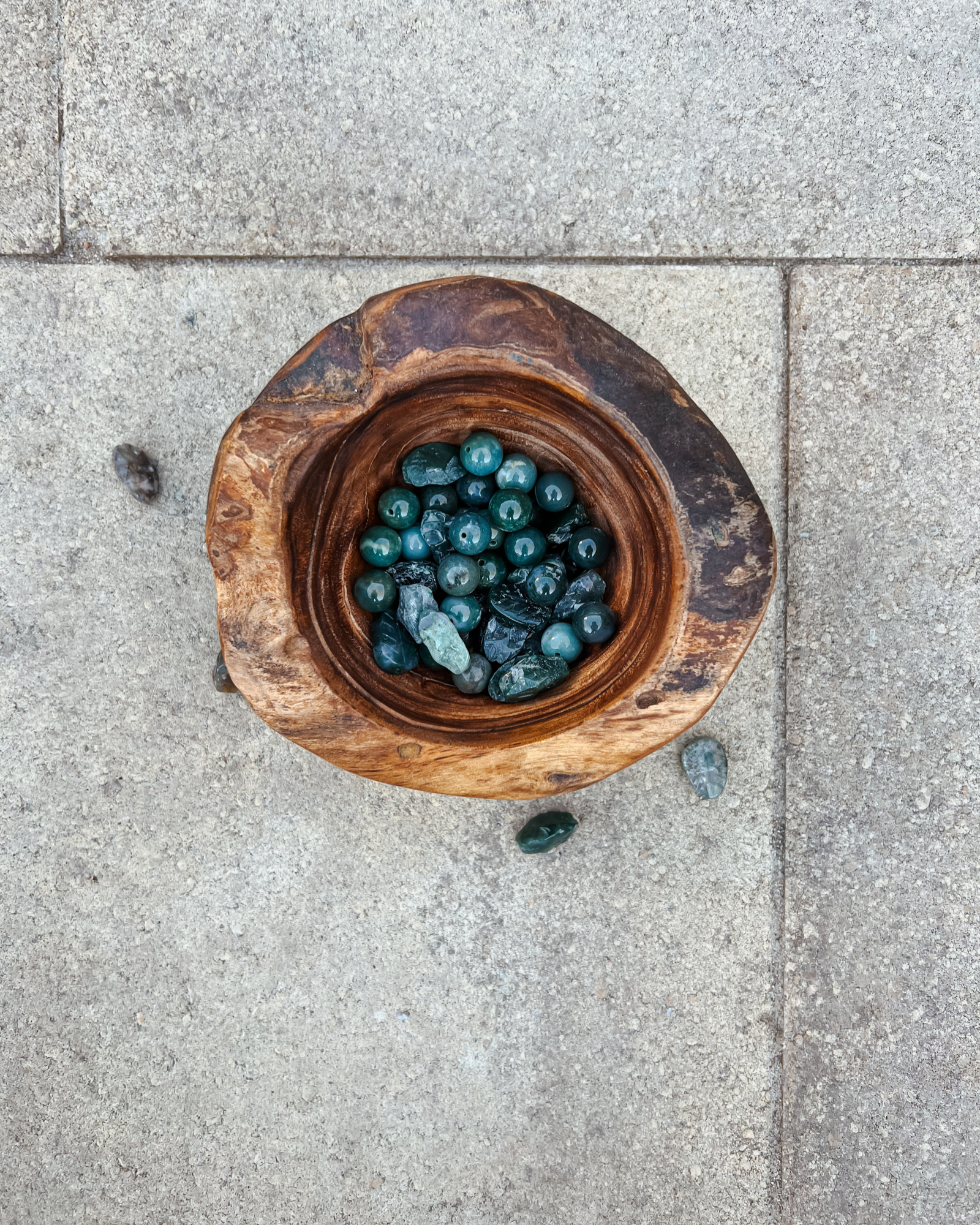 Photo of an overhead view of a wooden bowl full of moss agate crystals.