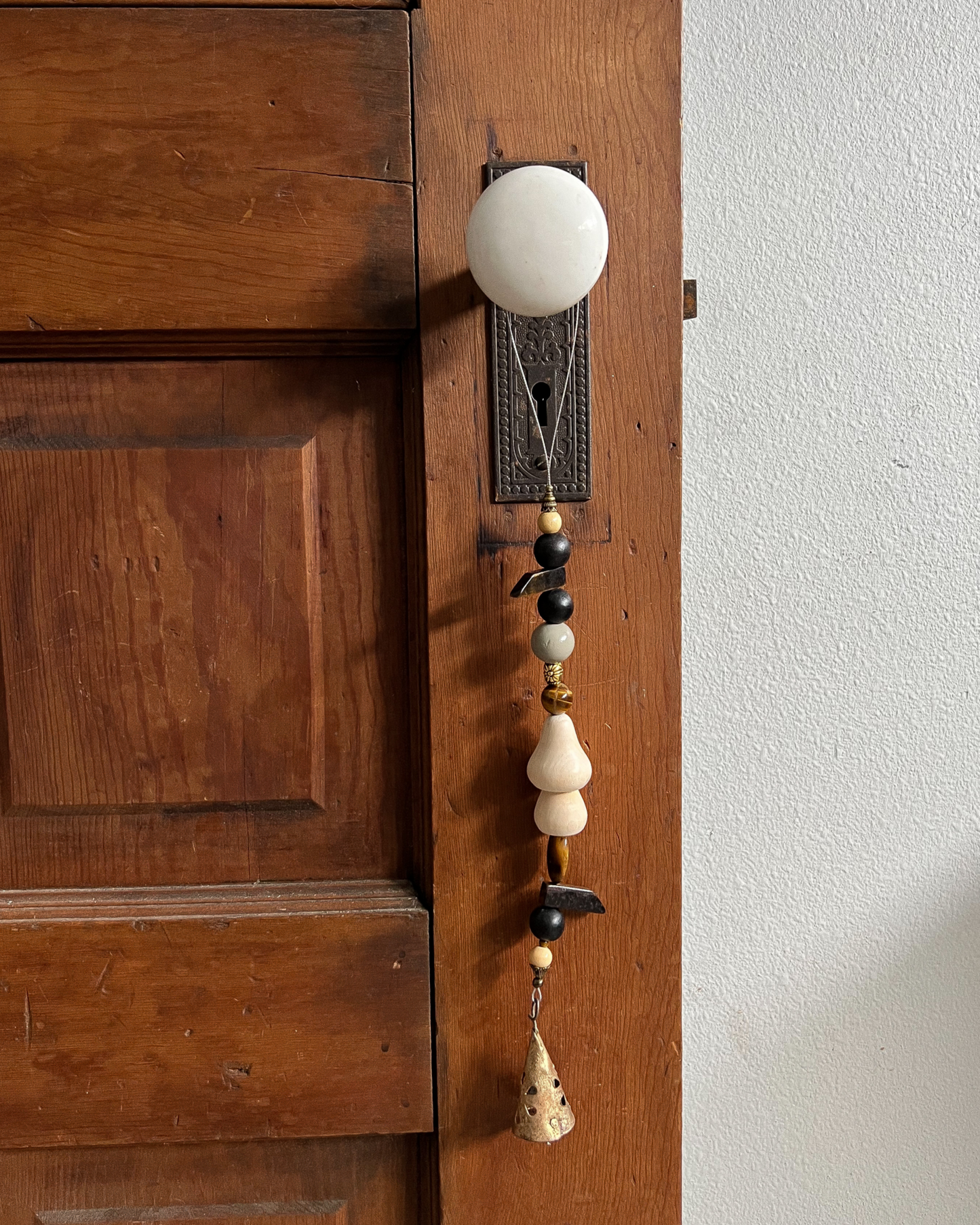 Single strand of wooden beads, tigers eye crystals, and a golden bell hang from an antique doorknob.
