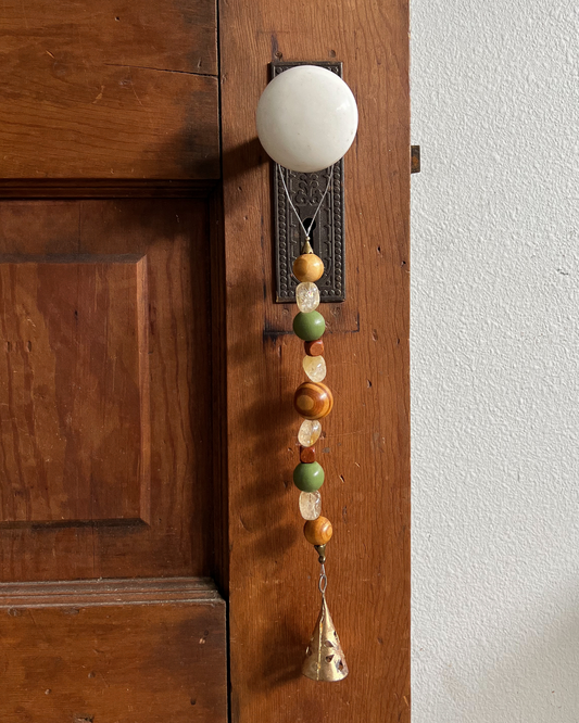 Single strand of wooden beads, citrine crystals, and a golden bell hang from an antique doorknob. 