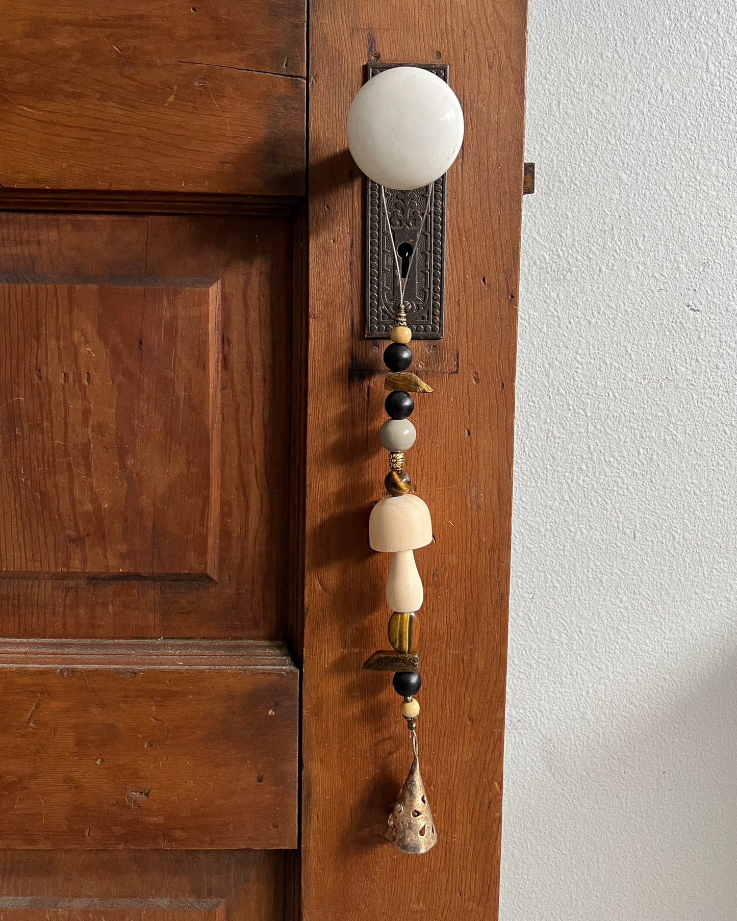 Single strand of wooden beads, tigers eye crystals, and a golden bell hang from an antique doorknob.