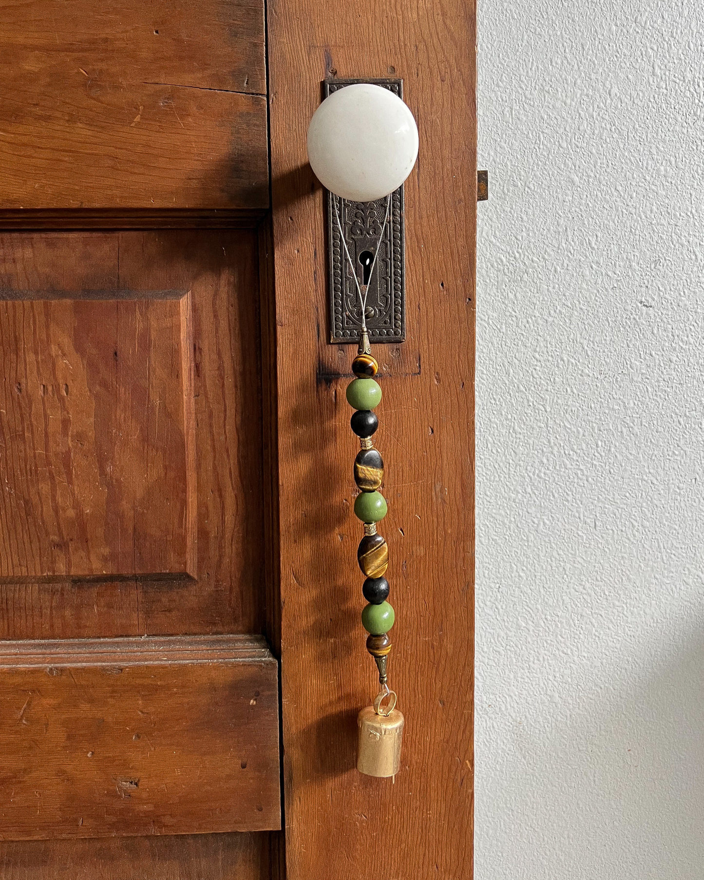 Single strand of wooden bells, tiger's eye crystals, and a golden bell hanging from an antique doorknob.