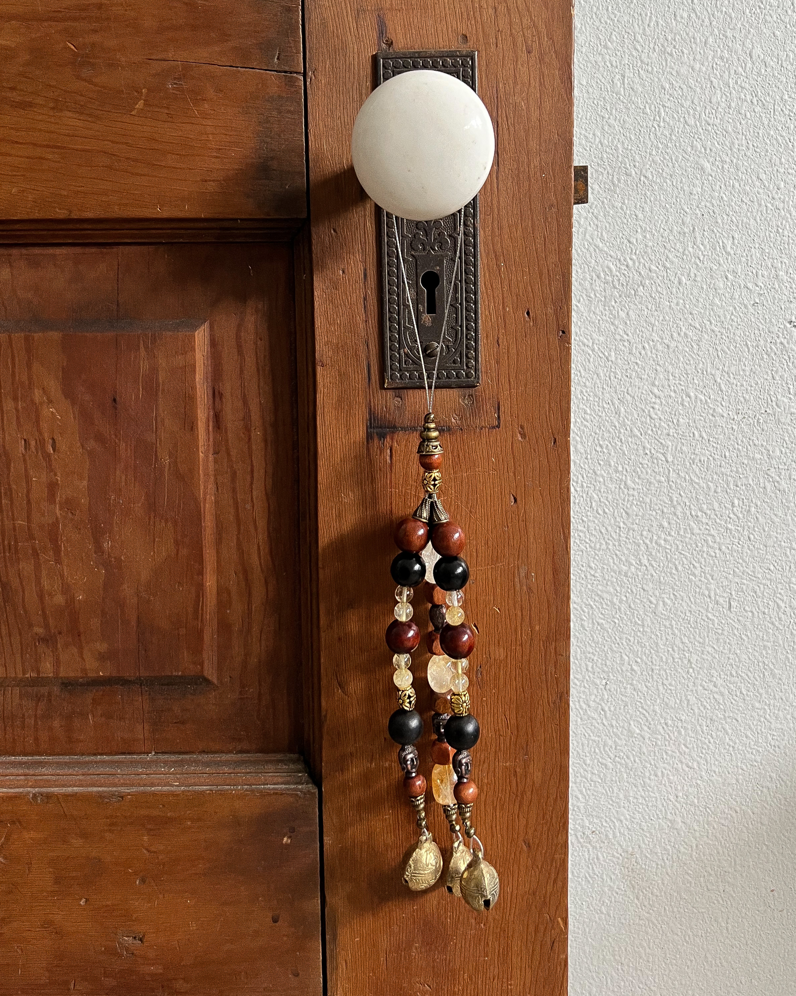 Triple strands of wooden bells, citrine crystals, metallic buddhas, and three golden bells hanging from an antique doorknob.