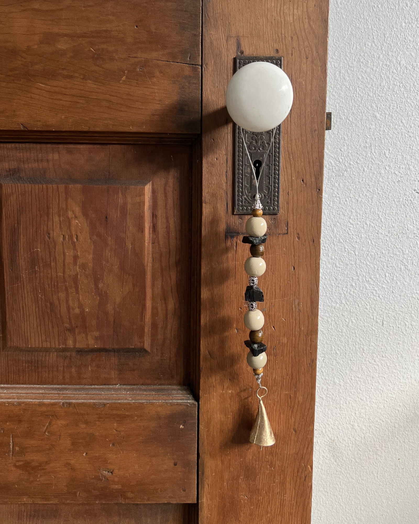 Single strand of wooden beads, black tourmaline crystals, and a golden bell hanging from an antique doorknob.