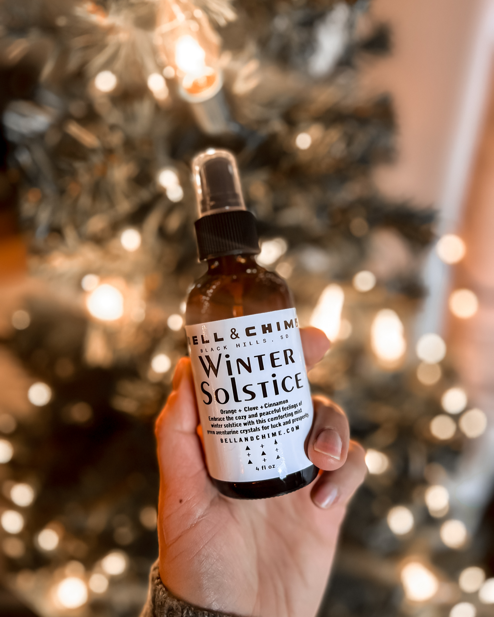 A person holds the Winter Solstice clearing spray in their hand in front of a Christmas tree.