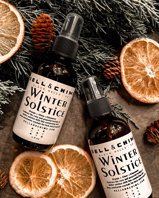 Two bottles of the Winter Solstice clearing spray lay amongst juniper bows, dehydrated orange slices, and pine cones.