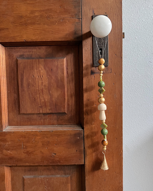 Single strand of wooden beads, serpentine crystals, and a golden bell hang from an antique doorknob.