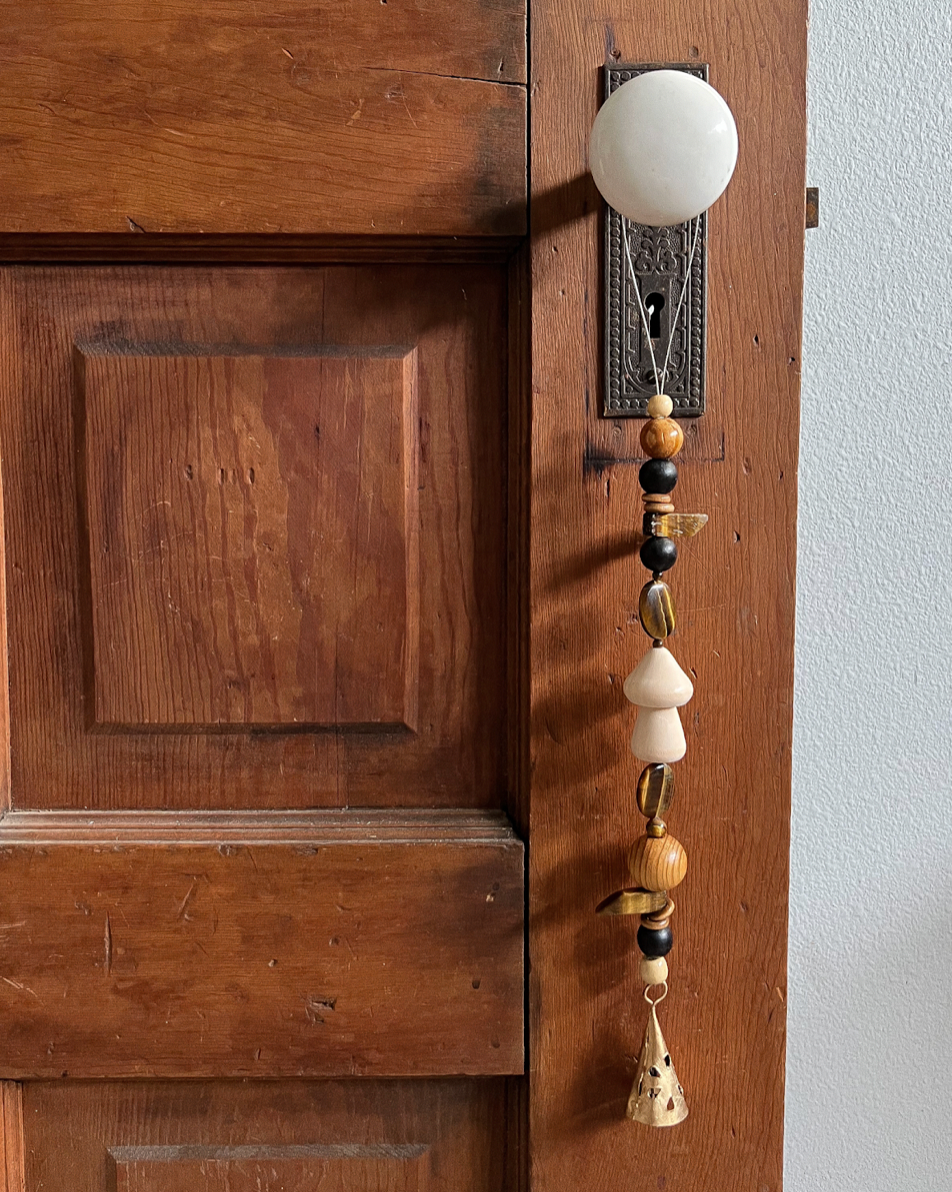 Single strand of wooden beads, tigers eye crystals, and a golden bell hang from an antique doorknob.