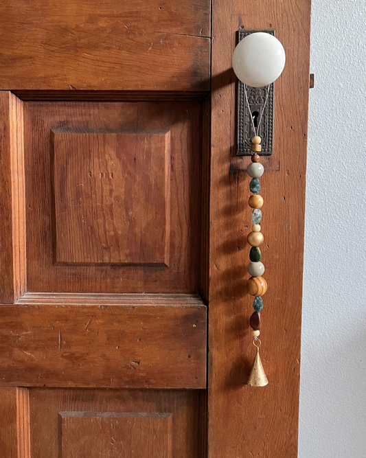 Single strand of wooden beads, moss agate crystals, and a golden bell hanging on an antique doorknob.