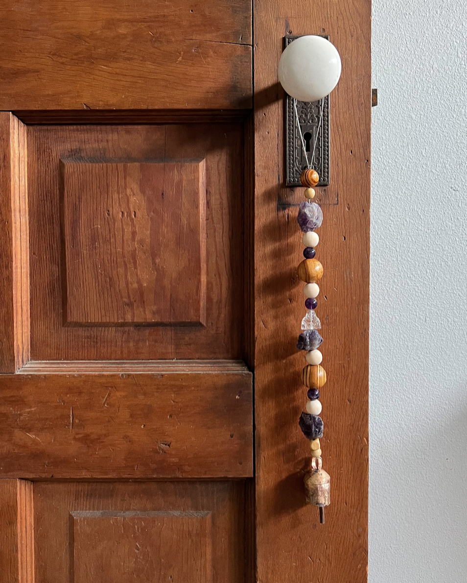 Single strand of wooden beads, amethyst crystals, and a golden bell hanging from an antique doorknob.