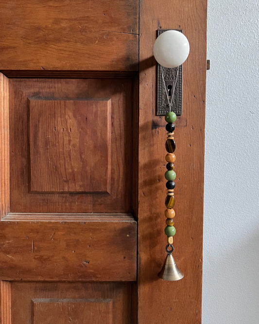 Single strand of wooden bells, tiger's eye crystals, and a golden bell hanging from an antique doorknob.