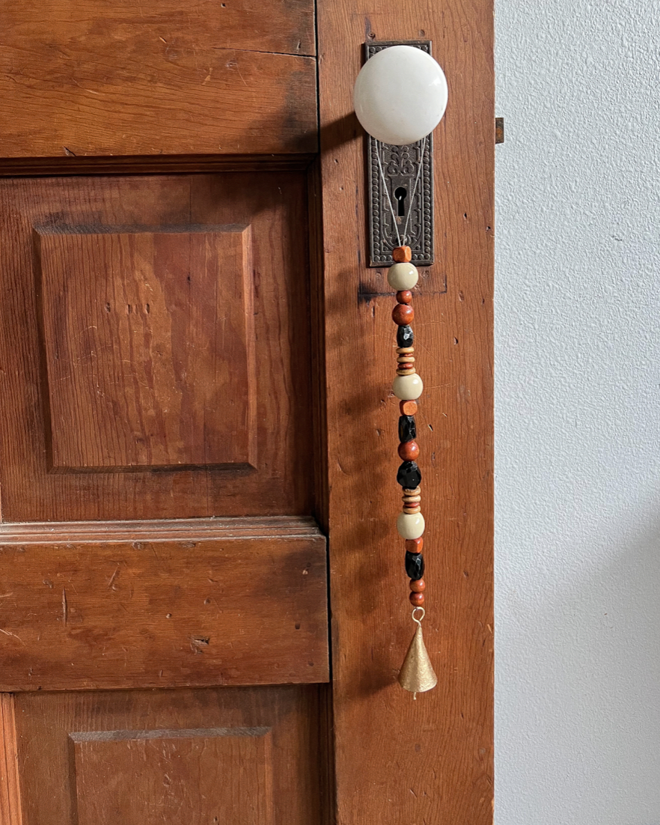 Single strand of wooden beads, black tourmaline crystals, and a golden bell hanging from an antique doorknob.