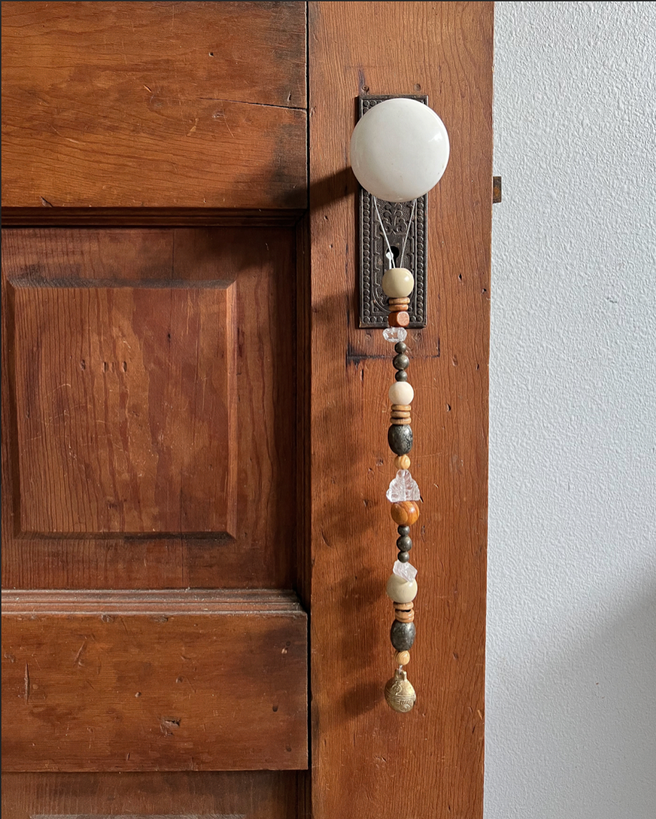 Single strand of wooden beads, pyrite crystals, a single clear buddha crystal, and a golden bell hanging from an antique doorknob.