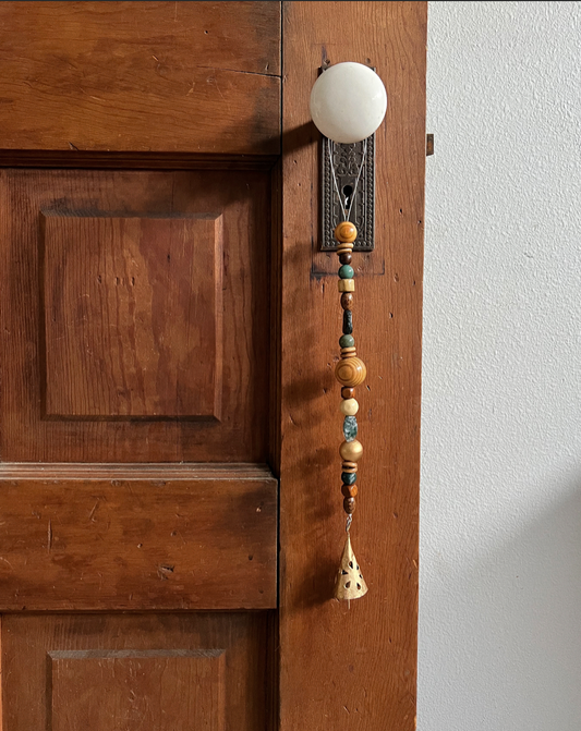 Single strand of wooden beads, moss agate crystals, and a golden bell hanging from an antique doorknob.