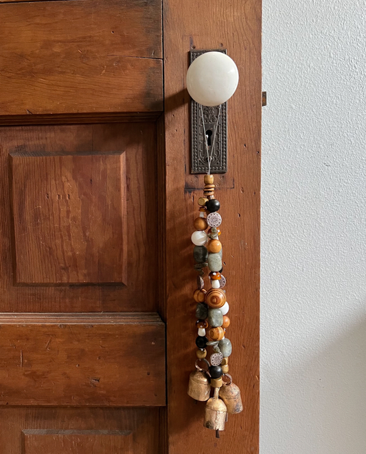 Triple strands of wooden beads, metal charms, mushroom beads, labradorite crystals, and three golden bells hanging from an antique doorknob.