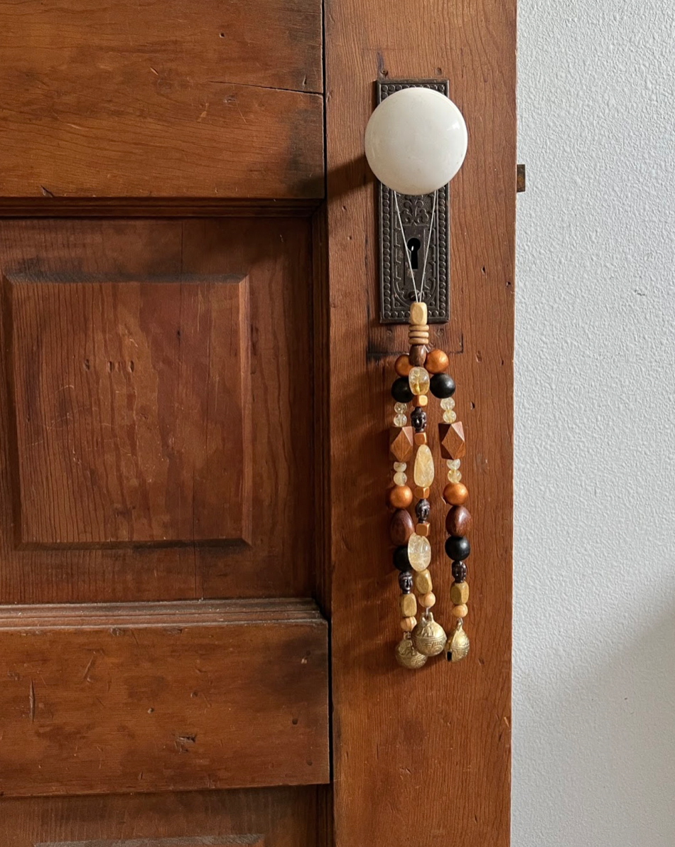 Triple strands of wooden bells, citrine crystals, metallic buddhas, and three golden bells hanging from an antique doorknob.