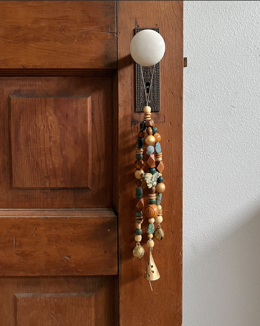 Triple strand of wooden beads, moss agate crystals, a single moss agate butterfly, and three golden bells hanging from an antique doorknob.