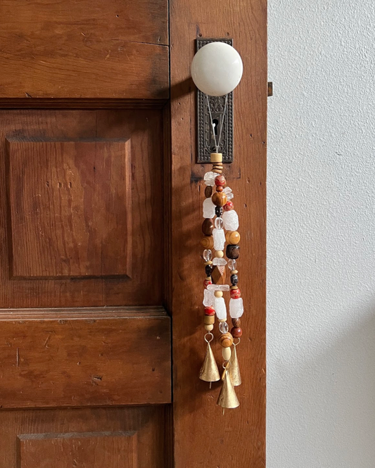 Triple strands of wooden beads, clear quartz crystals, metallic buddhas, and three golden bells hanging from an antique doorknob.