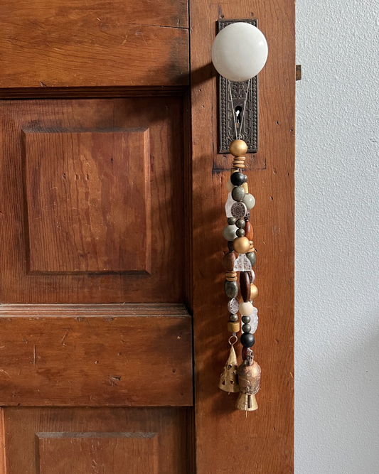 Triple strands of wooden beads, pyrite crystals, metal beads, a single crystal buddha, and three golden bells hanging from an antique doorknob.