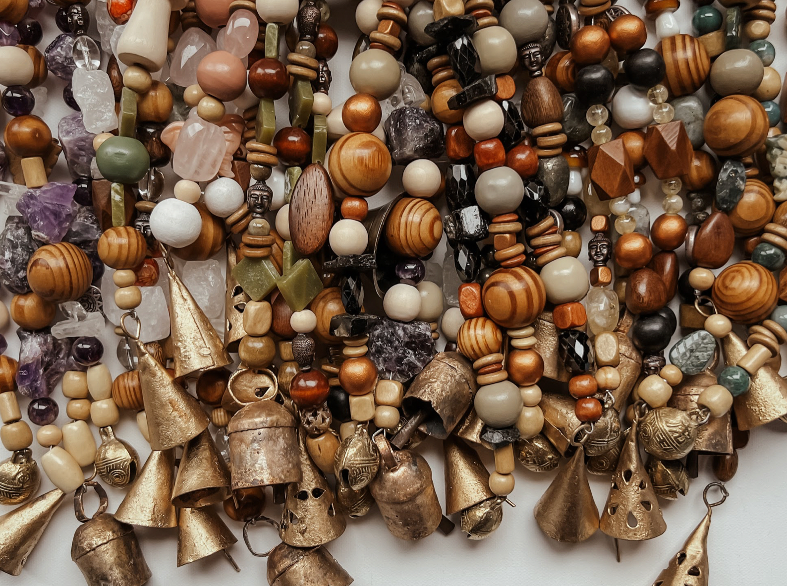 Overhead photo of single and triple strands of assorted gemstones, wooden beads, and antique golden bells laying on a table.